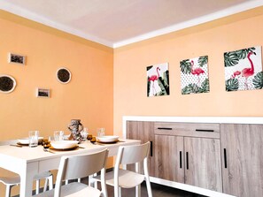 A dining area with a table set for four, white chairs, a wooden cabinet with two doors, and wall art featuring flamingos.