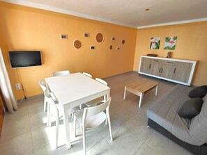 A living room with a white table, grey sofa, and a TV mounted on the wall.