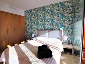A hotel room with a bed, a wooden wardrobe, a nightstand with a lamp, and a window with a view.