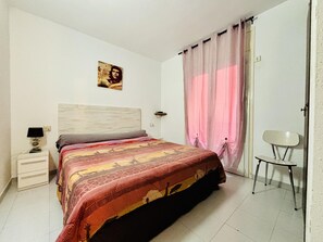 Un dormitorio con una cama, una mesita de noche, una silla, una lámpara de pared y un cartel.