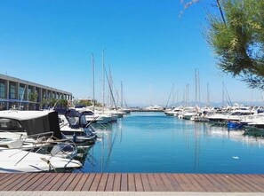 Un port de plaisance avec des bateaux amarrés, une terrasse en bois et, au fond, un bâtiment doté de grandes fenêtres.