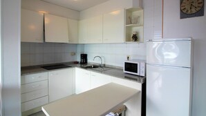 Una cocina moderna con gabinetes blancos, microondas integrado, cafetera y refrigerador.
