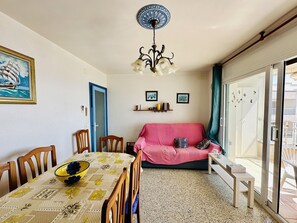 A dining area with a table, chairs, a chandelier, a pink sofa, and a glass door leading to an outdoor area.