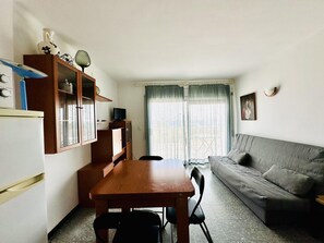 Un espace de vie compact comprenant un coin cuisine, une table à manger avec des chaises, un canapé et une fenêtre avec des rideaux.