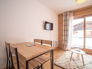 Quarto moderno com mesa de jantar de madeira, cadeiras, TV fixada na parede e vista de um prédio de madeira lá fora.
