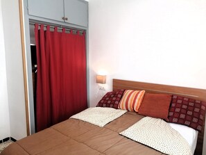 A bedroom with a bed, a nightstand, a lamp, and a wardrobe with a red curtain.