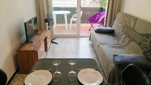 A living room with a sofa, a small wooden table, and a balcony with a chair and a table. - Charming Apt in Heart of Santa Margarida, Near Beach, Terrace, & Parking (Roses)
