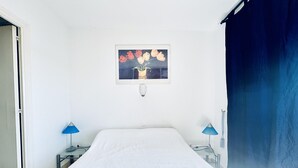 Quarto com uma cama, duas mesas de cabeceira, uma luminária na parede e um quadro de flores.