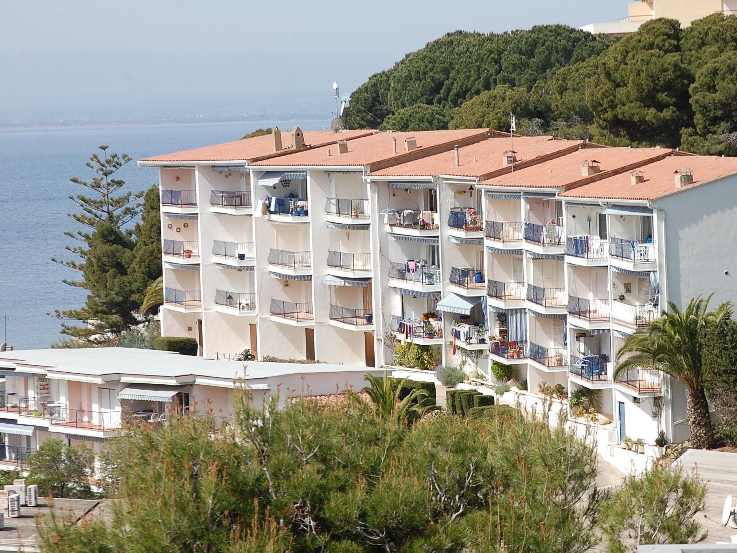 A multi-story hotel with balconies, a view of the sea, and a hilly backdrop.