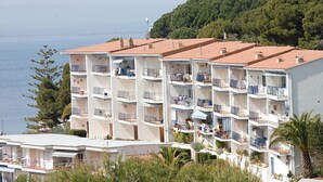 Hotel com vários andares, varandas, vista para o mar e um horizonte montanhoso.