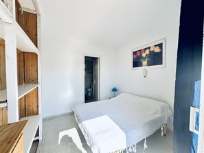 Un dormitorio con una cama, un cuadro, una puerta que da a un baño y estanterías de madera.