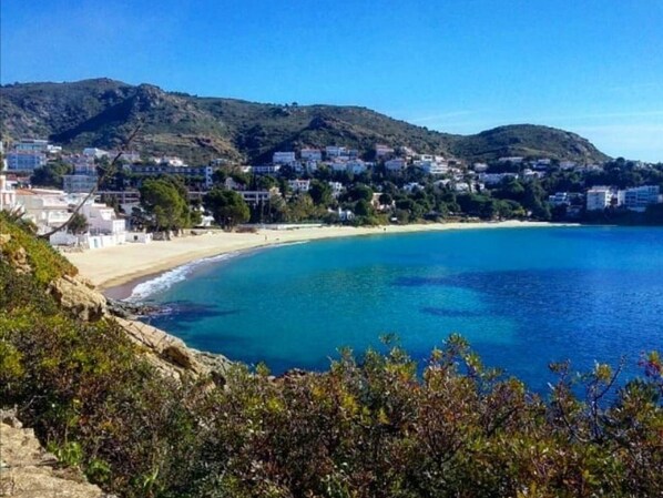 Un pueblo costero con playa, edificios y colinas al fondo.