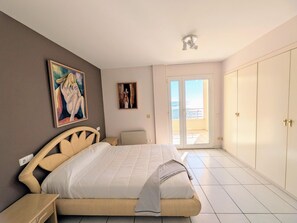 A bedroom with a bed, a painting, a nightstand, a chair, a wardrobe, and a door leading to a balcony.