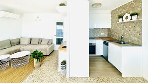 Eine moderne Wohnung mit Wohnbereich, ausgestattet mit einer Couch, einem Couchtisch und Zimmerpflanzen. Die Küche verfügt über weiße Schränke, eine Granitarbeitsplatte und eine Spritzschutzleiste mit einem gefleckten Muster.