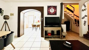 A living room with a TV, a tripod, a clock, and a staircase. - Charming House Near Natural Park - Hiking, Biking, Windsurfing & Communal Pool (Roses)