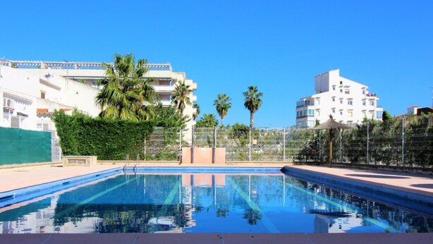 A swimming pool with clear blue water, surrounded by a tiled deck. There are palm trees and a fence in the background. - Charming House Near Natural Park - Hiking, Biking, Windsurfing & Communal Pool (Roses)