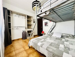 Ein Schlafsaalzimmer mit Etagenbetten, einem Kleiderschrank, einem kleinen Tisch mit einer roten Tasse und einer Leiter zum oberen Bett.