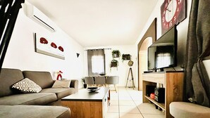 A modern living room with a sofa, coffee table, TV, and a tripod. - Charming House Near Natural Park - Hiking, Biking, Windsurfing & Communal Pool (Roses)