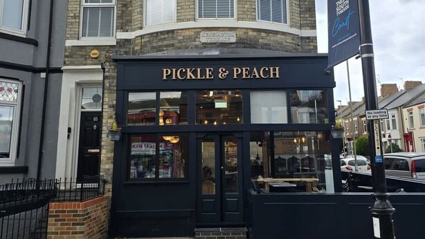 Rakennuksen sisäänkäynnin yläpuolella on kyltti, jossa lukee: ”PICKLE & PEACH”.