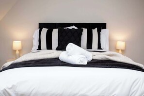 A neatly made bed with a black and white striped headboard, white pillows, and a rolled white towel. - Vacant Nests - The Ocean Retreat (South Tyneside)