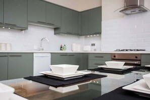 A modern kitchen with green cabinets, white countertops, and a glass-top dining table. - Vacant Nests - The Ocean Retreat (South Tyneside)