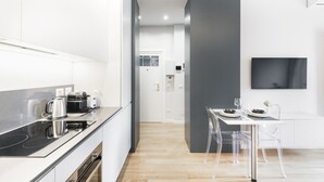 A modern kitchen with a black countertop, stainless steel appliances, and a dining area with a table and chairs. - Easylife - Modern studio in the heart of Navigli (Milano)