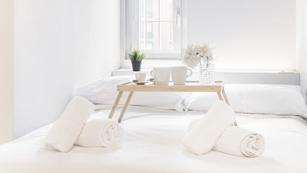 A neatly made bed with white linens and towels, a tray with cups and a vase of flowers, and a potted plant by the window. - Easylife - Modern studio in the heart of Navigli (Milano)