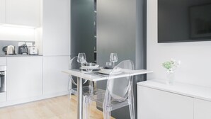 A modern kitchen with white cabinetry, a dining table with clear chairs, and a small vase with flowers on the counter. - Easylife - Modern studio in the heart of Navigli (Milano)