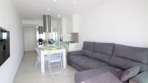 A modern living space with a dining area, a grey sofa, and a kitchen in the background. - Cozy studio with terrace and included parking (Roses)