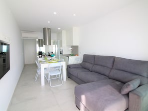 Un espacio de estar moderno con comedor, un sofá gris y una cocina al fondo.
