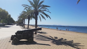 A beach with a cannon on the left, palm trees, and a clear blue sky. - Cozy studio with terrace and included parking (Roses)