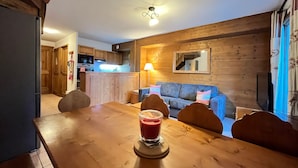 A cozy living room with a wooden dining table, a sofa, and a kitchen in the background.