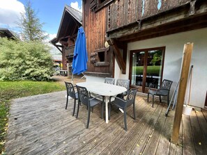A wooden deck with a table and chairs, a blue umbrella, and a building with a balcony.