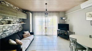 A living room with a sofa, TV, dining table, and a view of the outdoors through a glass door. - Bright apartment with sea view, pets allowed (Roses)