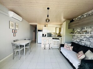 A compact living space with a dining area, kitchenette, and a sofa with patterned cushions. - Bright apartment with sea view, pets allowed (Roses)