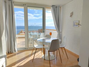 A balcony with a table and chairs, a view of the sea, and a white interior.