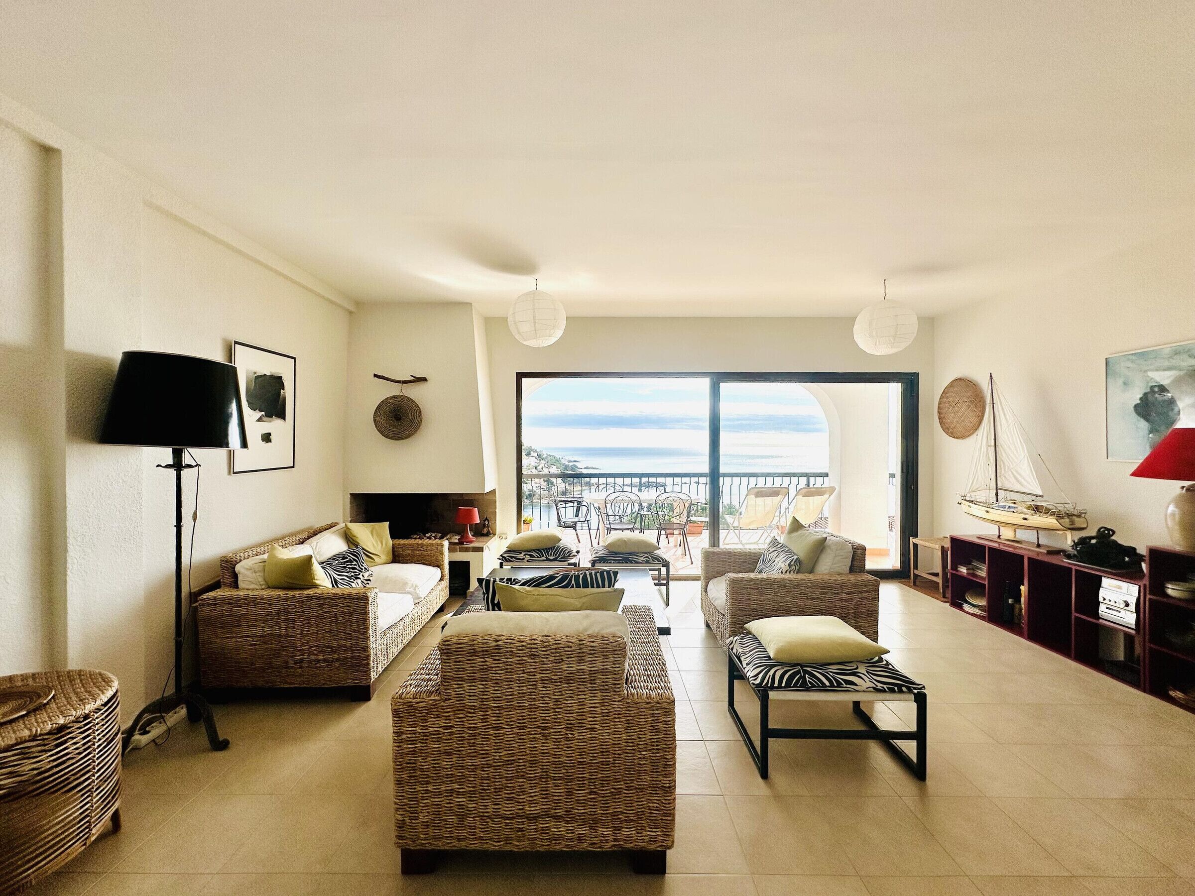 A spacious living room with wicker furniture, a fireplace, and a view of the sea.