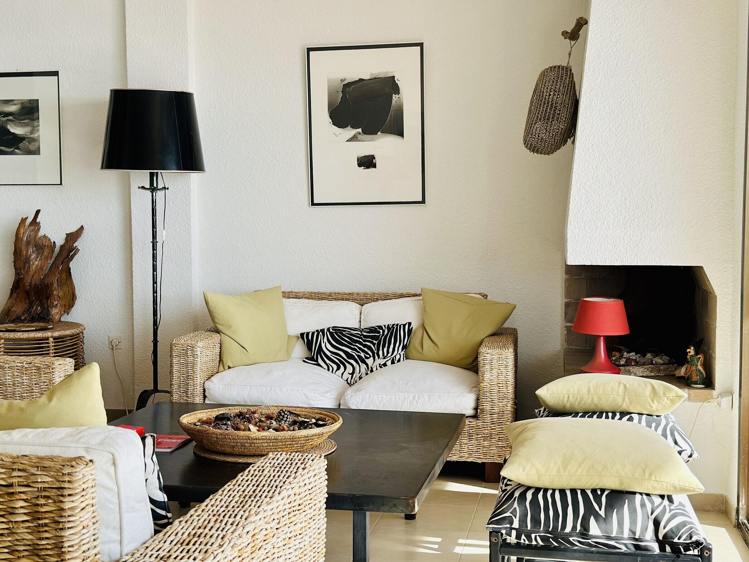 Una sala de estar acogedora con muebles de mimbre, una chimenea y un cuadro en la pared.