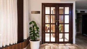 Un hall d’hôtel avec une porte en bois, une plante en pot et un panneau indiquant l’emplacement du café.