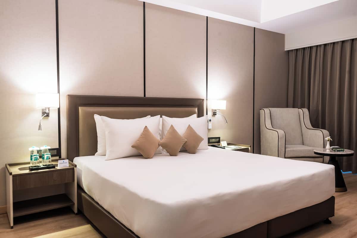 Ein Hotelzimmer mit einem großen Bett, zwei Nachttischen, einem Sessel und einem kleinen Tisch.