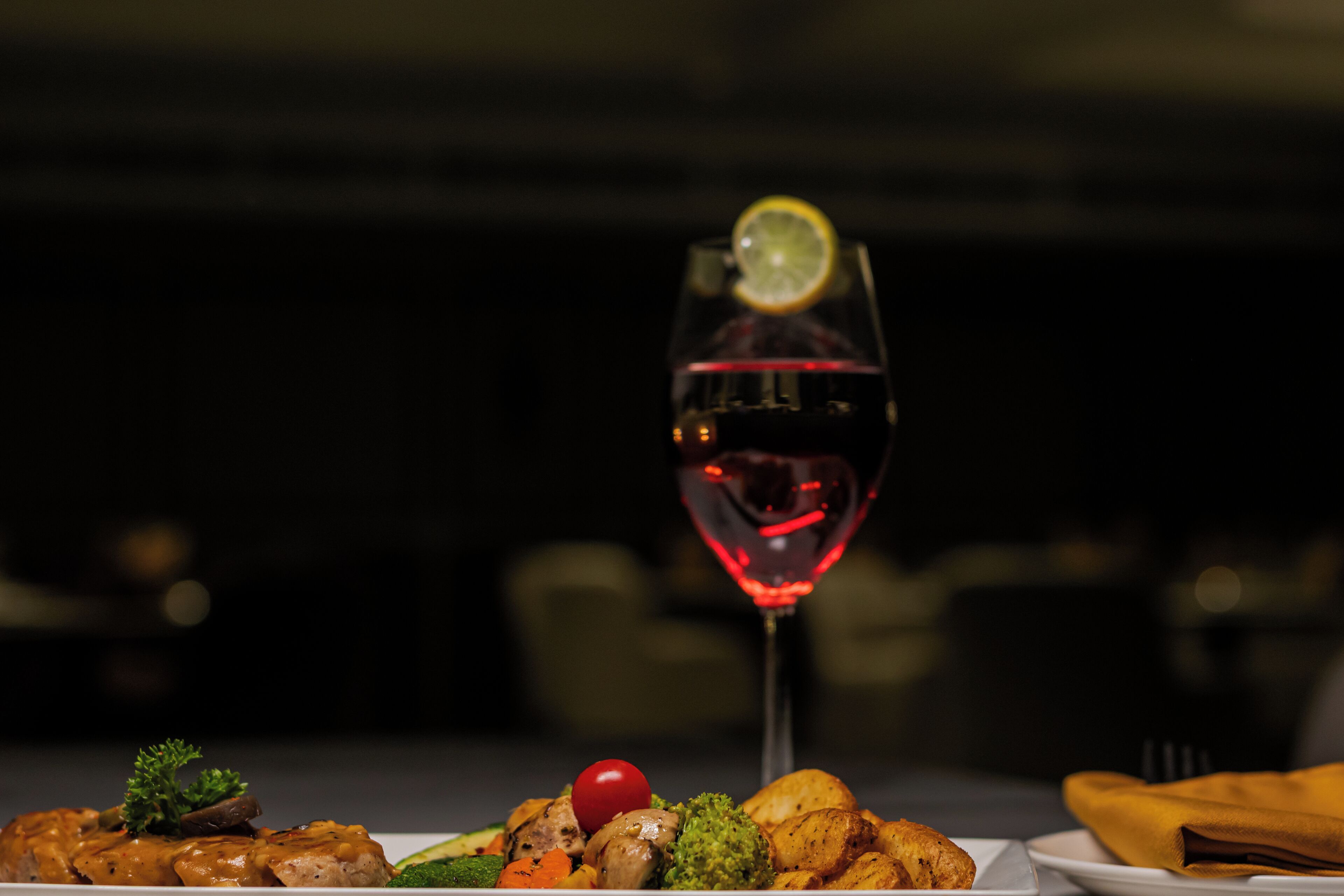 A dining table with a plate of food and a glass of red wine.