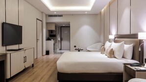 Une chambre d’hôtel moderne dotée d’un grand lit, de tables de chevet, d’un téléviseur à écran plat et d’un coin salon séparé avec une chaise et une table.