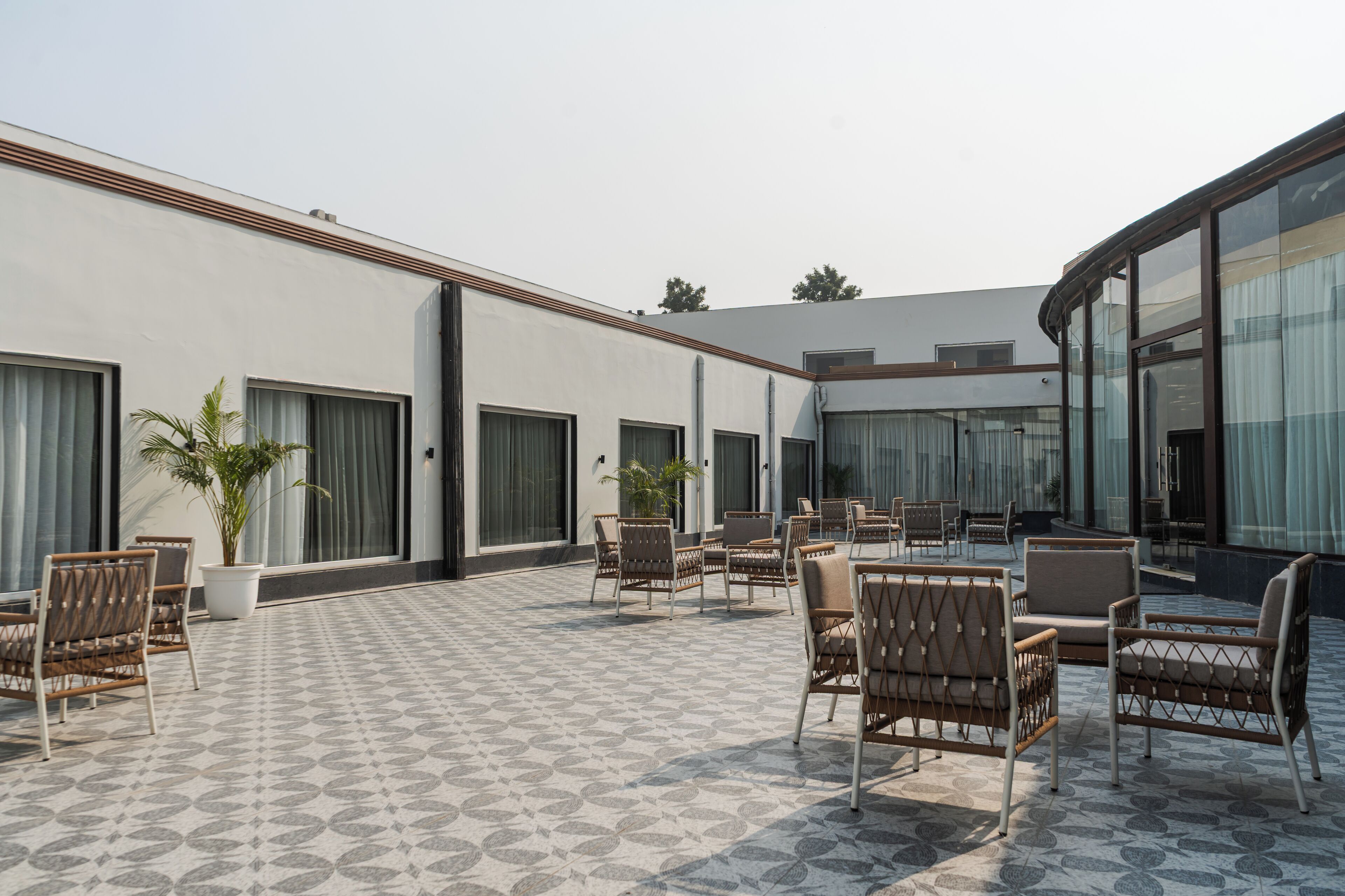 A modern outdoor seating area with wicker chairs and a patterned floor, surrounded by large windows and a building facade.