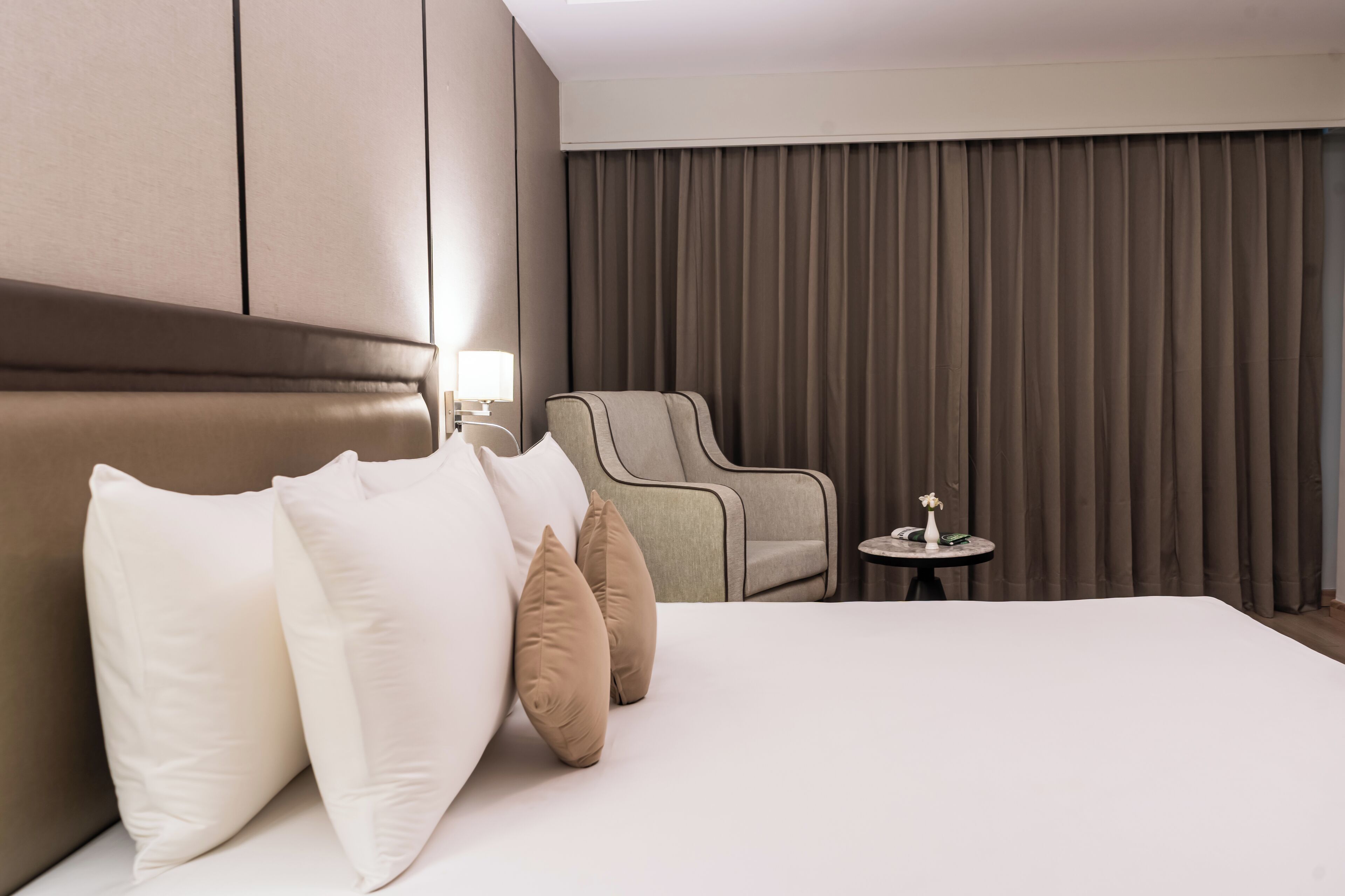 Una habitación de hotel con una cama grande, una zona de estar con una silla y una mesita, y un ventanal con cortinas.