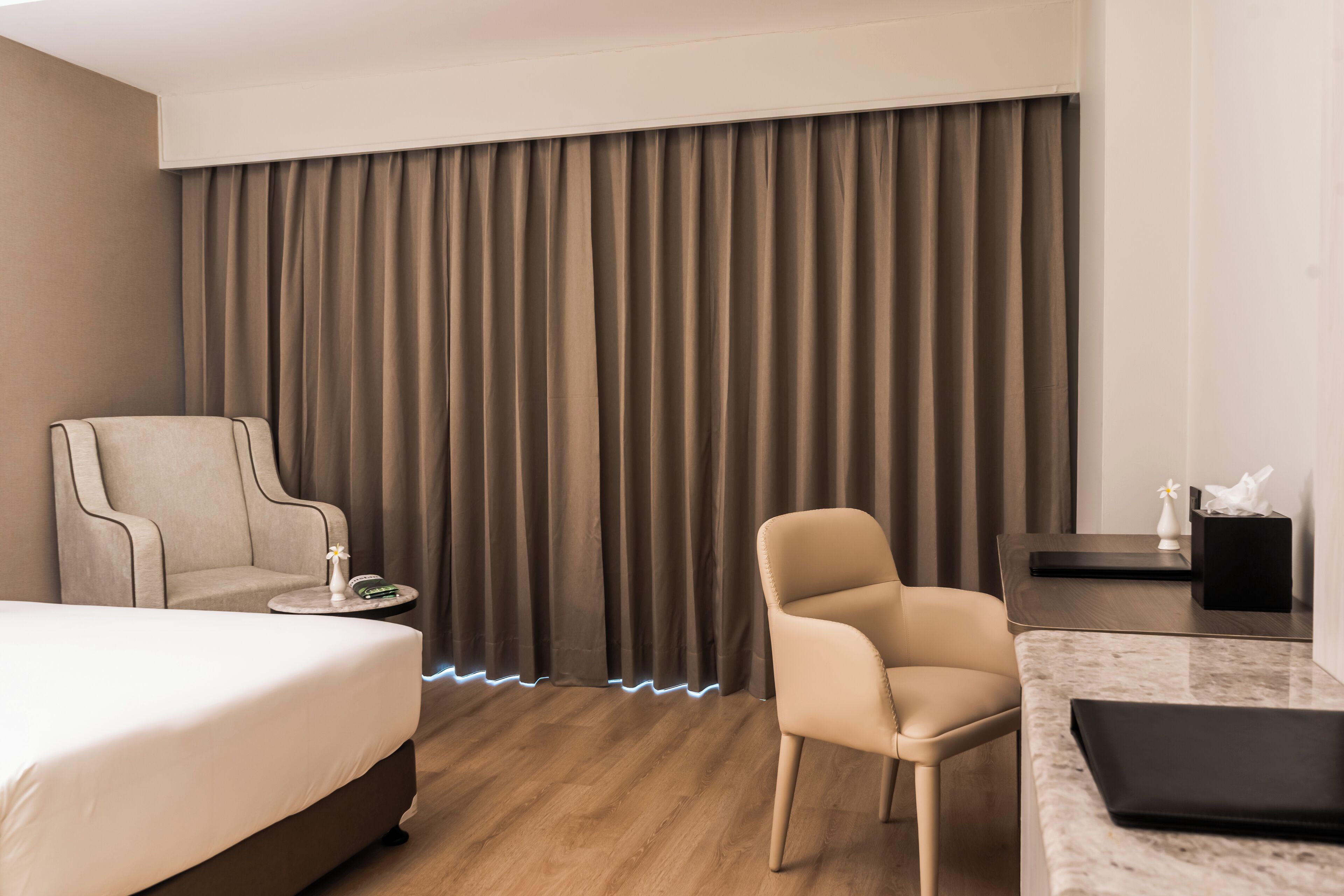 A modern hotel room with a bed, two armchairs, a small round table, and a desk with a laptop.