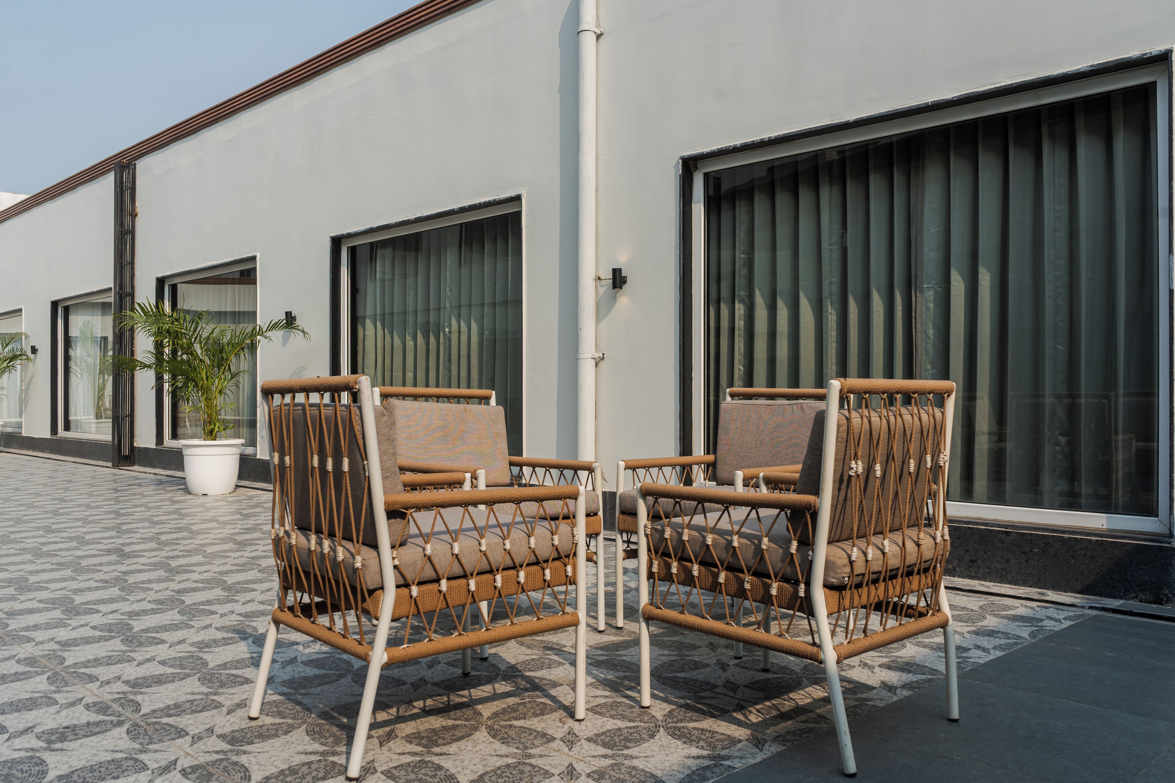 Two wicker chairs with cushions, a potted plant, and a building with large windows and a tiled floor.
