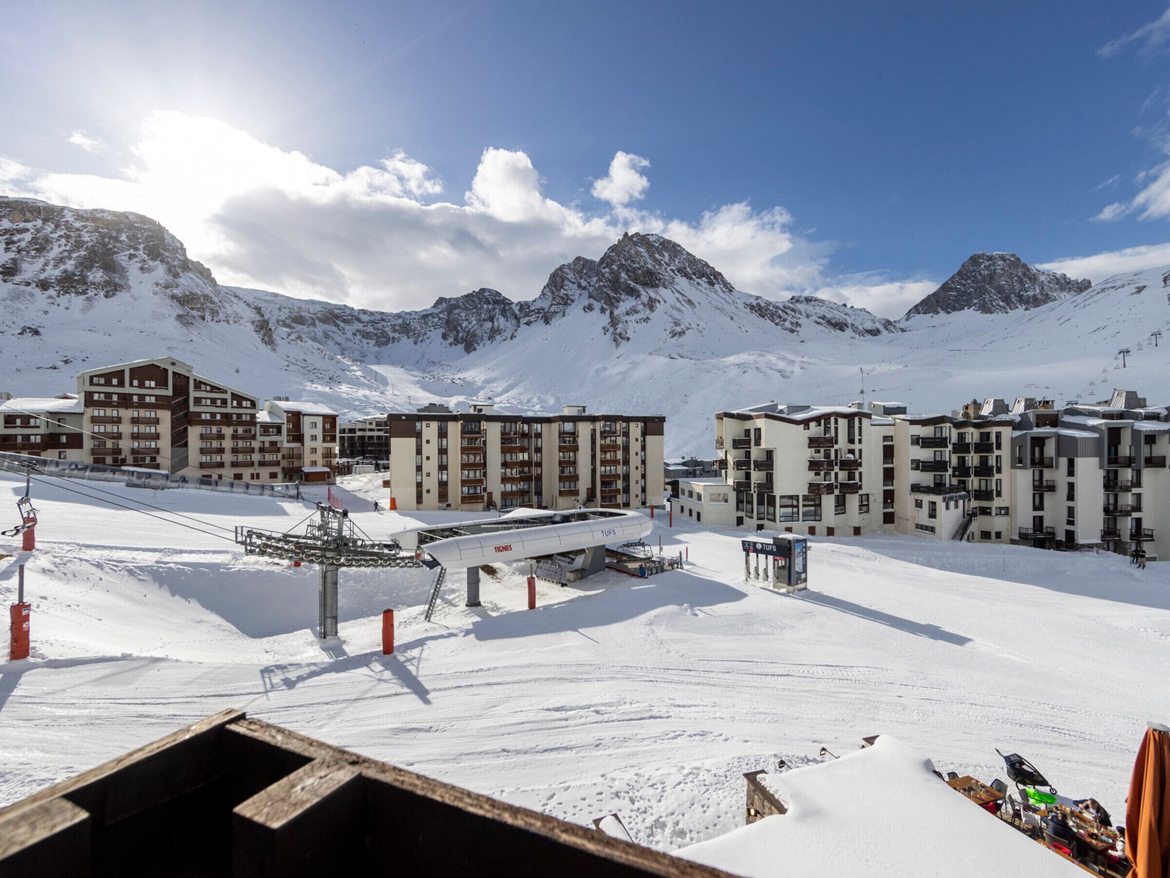 A snow-covered ski resort with modern buildings, ski lifts, and a mountain backdrop.