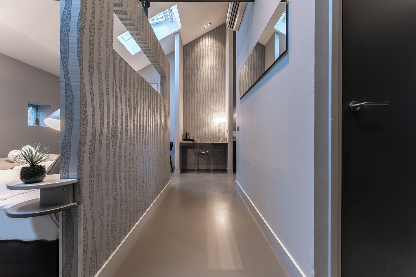 A modern hallway with a curved ceiling, a small seating area with a plant, and a view of a bathroom with a sink and mirror.