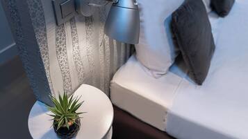 A neatly made bed with pillows, a bedside lamp, and a small potted plant on a round table beside the bed.