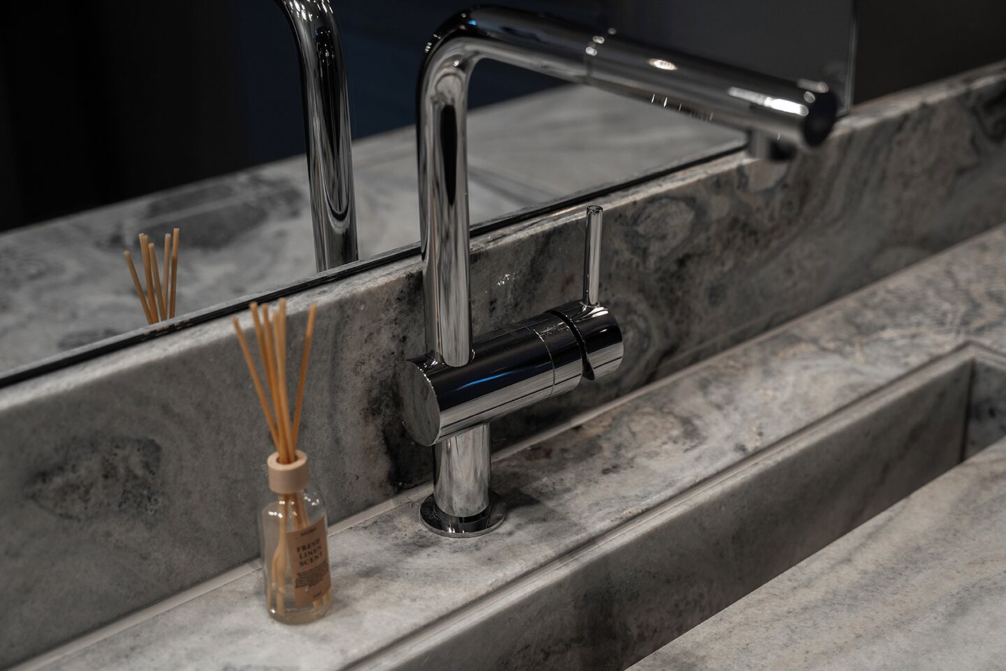 A modern bathroom with a marble countertop, a chrome faucet, and a glass bottle of reed diffuser.